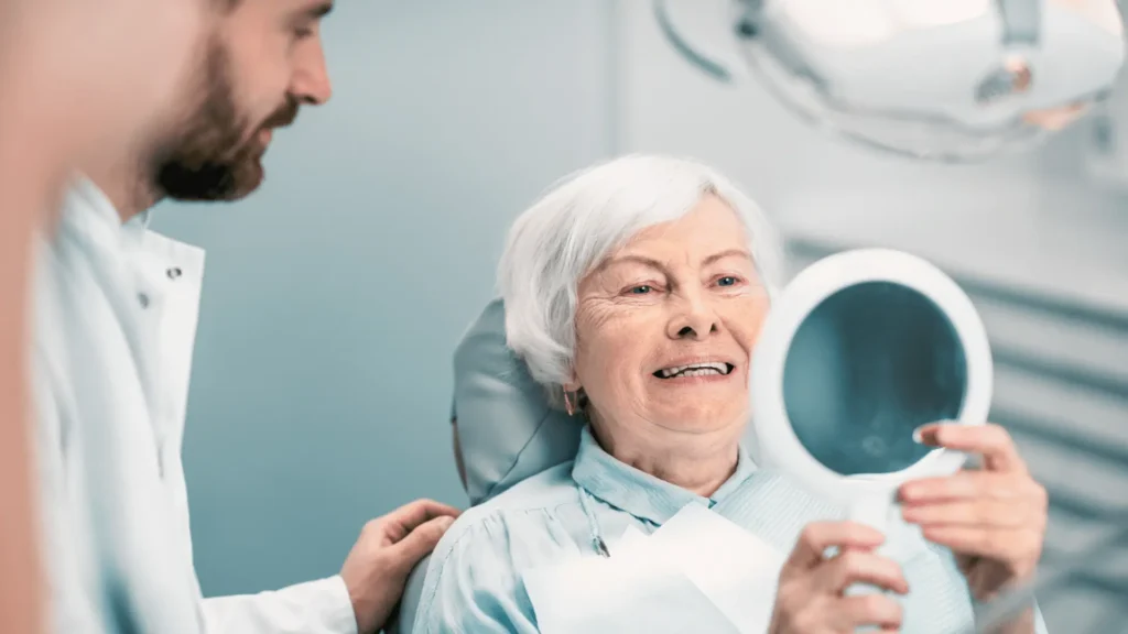 Усмихната възрастна жена щастлива след оперативна интервенция по поставянето на зъбни импланти и последващото им въвеждане във функция